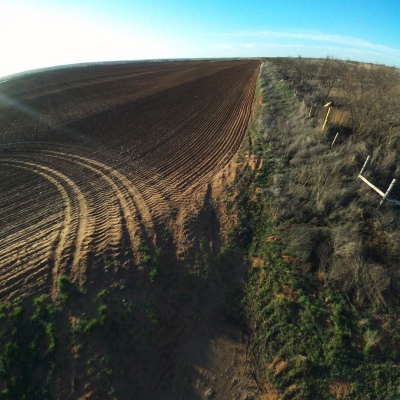 Photo of tilled soil with tire tracks turning away from a weedy field